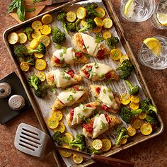 a pan filled with fish covered in cheese and veggies next to wine glasses