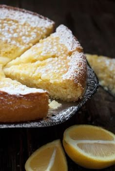 a lemon cake with powdered sugar on top and sliced lemons next to it