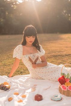 a woman is sitting on a blanket in the grass with some pastries and donuts