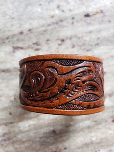 "This wrist band is made from heavy vegetable tanned cowhide with heavy duty snaps for years of wear. It is 1-1/4 \" wide and made to fit your wrist. The band is stained and a protective finish is used to add extra life. The edges have been hand rubbed to a super smooth finish that won't irritate you. To get your correct size measure around your wrist with a flexible tape measure or use a string and measure string with a ruler." Leather Cuff Bracelet Diy, Cuff Bracelets Diy, Leather Ideas, Tan Cowhide, Wrist Band, Hand Tooled Leather, Leather Bracelets, Leather Cuffs Bracelet, Tooled Leather