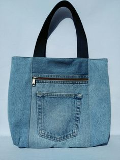 a blue jean purse with black handles and zippers on the front, sitting against a white background