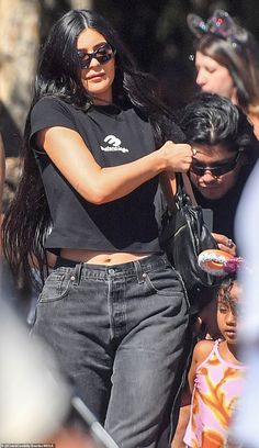 a woman with long black hair and sunglasses is holding onto a handbag as she walks down the street