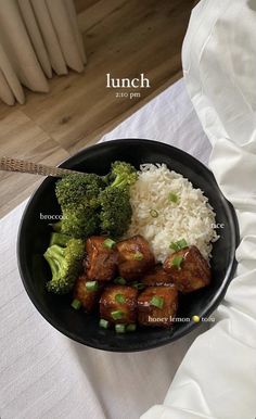 a black plate topped with meat and broccoli on top of a white table cloth