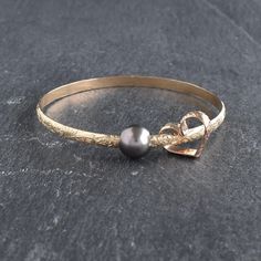 Price is per bangle. Multiple bangles are sold separately.  4mm Hawaiian Heirloom style bangle bracelet with a free moving Tahitian Pearl and a matching hand bent and soldered heart charm.  Two shape of Tahitian pearl available: 1. Tahitian pearl is round in shape, approximately 10-10.5mm in size. Some minor dimples/blemishes may be visible on the back or side of pearl. We choose a clean face for the front of the pearl facing outwards from the bangle.  2. Oval shape Tahitian pearl with or withou Luxury Tahitian Pearl Jewelry Gift, Luxury Gold Rings With Tahitian Pearl, Elegant Luxury Tahitian Pearl Bracelets, Luxury Tahitian Pearl Jewelry With Pearl Charm, Luxury Tahitian Pearl Charm Jewelry, Pearl Bangles Gold, Hawaiian Heirloom Jewelry, Tahitian Pearls Jewelry, Heart Bangle Bracelet