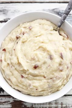 a white bowl filled with mashed potatoes on top of a wooden table next to a fork