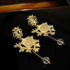 Description: The earrings feature a gold-plated base with a delicate, intricate design resembling branches and leaves. At the center of each earring, a stunning frozen rose is featured. Dangling from the bottom of each earring is a crystal bead, adding to the overall elegance and sophistication of the piece. The earrings would make a beautiful and unique addition to any jewelry collection. Product Details: -Royal Vintage Design -925 silver post -Gold plated Base -Imitation crystal Measurement: 3"length x 1 1/2"widest Elegant Rose Gold Flower Clip-on Earrings, Rose Gold Flower Jewelry For Evening, Elegant Rose Gold Flower Earrings For Evening, Gold Crystal Flower Shape Earrings For Parties, Gold Flower Earrings For Formal Occasions, Elegant Rose Gold Pierced Crystal Earrings, Elegant Gold Flower Earrings For Formal Occasions, Elegant Gold Flower Clip-on Earrings, Rose Gold Pierced Flower Earrings For Formal Occasions