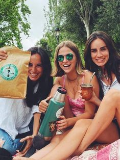 three young women sitting on the ground with their drinks and paper bags in front of them