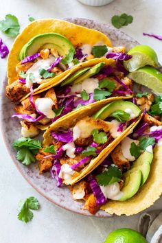 three fish tacos with cabbage, avocado and cilantro on a plate