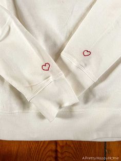 a white sweater with hearts embroidered on the chest and sleeves, sitting on a wooden floor