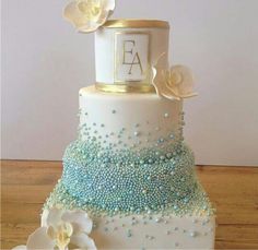 a white and blue wedding cake with flowers on the top is sitting on a wooden table