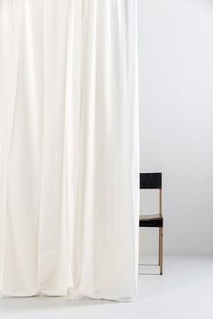 a white shower curtain sitting next to a black chair in a room with no curtains