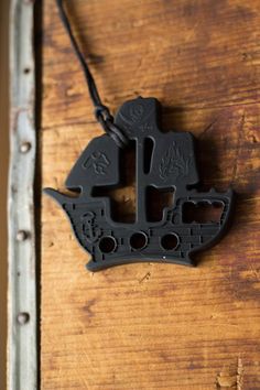 a black necklace with an image of a ship on it's front end, hanging from a wooden surface