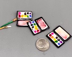 three miniature paints and a penny on a table with paintbrushes, one is empty