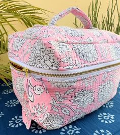 a pink and white floral print cosmetic bag on a blue tablecloth next to a potted plant