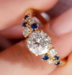 a woman's hand holding an engagement ring with blue and white stones on it