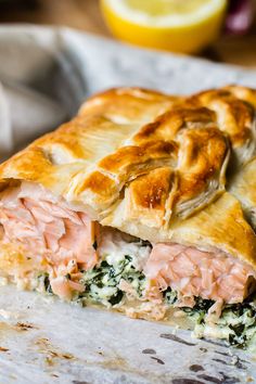 a piece of salmon and spinach pie on top of parchment paper with lemons in the background