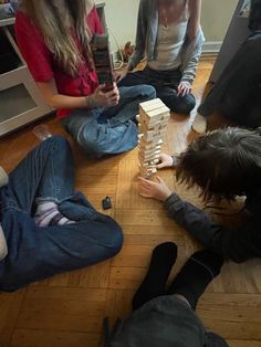 three people sitting on the floor playing with wooden blocks and building them into cubes