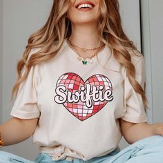 Get your groove on in our Swiftie Disco Heart Tee! This playful tee features a heart design inspired by the legendary icon. Perfect for any fan, this tee will have you dancing to your favorite tunes with style and flair. Rock out in our Swiftie Disco Heart Tee today! Size Guide: we recommend your true size for a loose fit or size down for a fitted fit. Tees are Unisex. Heather blend shirts are 52/48 Cotton/ Poly Blend and Shirts are Unisex. BELLA UNISEX TEE SIZING: Small - Length, 28" Width, 18" (4/6) Medium - Length, 29", Width, 20" (8/10) Large - Length, 30", Width, 22" (12/14) XLarge - Length, 31", Width, 24" (16/18) 2XLarge- Length, 32", Width, 26" (20/22) We recommend comparing these measurements against a shirt that you like the fit of for ordering a tee that will fit best. Crafted J Trendy Heart-shaped Tops With Graphic Print, Spring Heart Graphic T-shirt For Streetwear, Heart Graphic T-shirt For Spring Streetwear, Trendy T-shirt With Heart Graphic, Trendy Heart-shaped T-shirt For Spring, Spring Heart Graphic Tee, Spring Heart-shaped Graphic Tee, Retro White T-shirt With Heart Graphic, Heart-shaped Graphic Print T-shirt For Streetwear