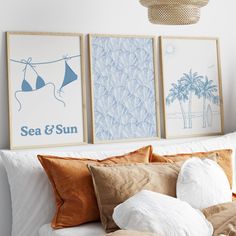 three framed pictures hang on the wall above a bed with white sheets and brown pillows