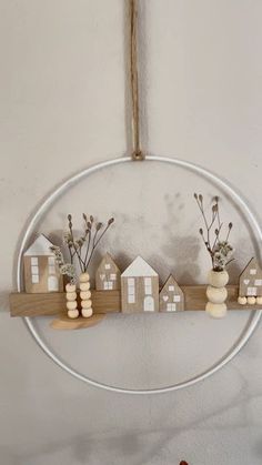 a white circle hanging on the wall with wooden houses and branches in it, along with two small vases filled with flowers