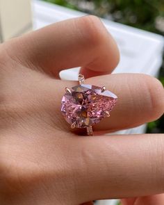 a woman's hand holding a pink diamond ring with diamonds on it and the center stone in the shape of a heart