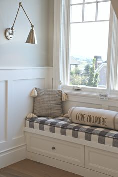 a window seat with two pillows on it in front of a window and a lamp