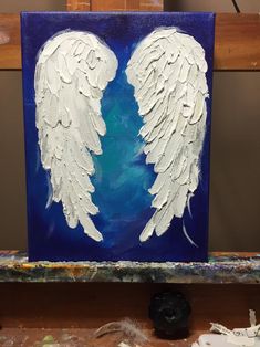 an acrylic painting of two white angel wings on a blue and purple background