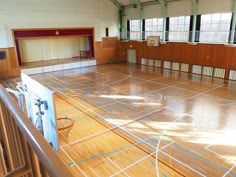 an indoor basketball court with hard wood flooring and wooden railings, surrounded by windows