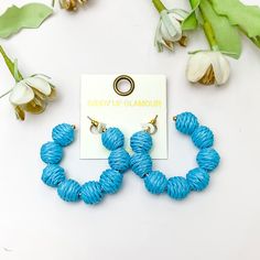 Sorbet Summer Raffia Ball Hoop Earrings in Blue. Pictured on a white background with flowers above the earrings. Trendy Blue Jewelry For Spring, Blue Hoop Earrings For Spring, Adjustable Hoop Earrings For Summer, Summer Beach Hoop Earrings, Adjustable Small Hoop Earrings In Blue, Adjustable Small Blue Hoop Earrings, Bohemian Small Hoop Earrings For Beach, Trendy Hoop Earrings For Vacation, Spring Vacation Hoop Earrings