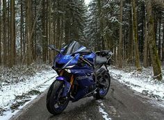 a blue motorcycle parked on the side of a snowy road in front of some trees