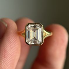 a close up of a person's hand holding a ring with an emerald stone