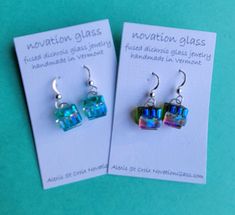 pair of earrings with blue and green glass cubes on them sitting next to each other