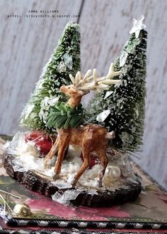 a deer figurine sitting on top of snow covered ground next to evergreen trees