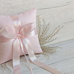 a pink pillow with a ribbon tied around it on top of a wooden floor next to a plant