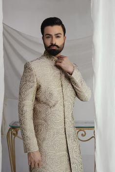 This light brown sherwani features intricate thread jal and a silk inner kurta pajama, paired with a tissue silk Rajasthani kula (turban) and a ruby stone brooch. Elevate your style with this royal look, perfect for special occasions. 4-Piece Suit Elegant Raw Silk Sherwani With Traditional Drape, Elegant Raw Silk Sherwani With Dabka Detailing, Beige Raw Silk Sherwani With Dabka, Elegant Embroidered Jamawar Bandhgala, Elegant Raw Silk Bandhgala With Intricate Embroidery, Beige Raw Silk Sherwani For Eid, Elegant Naqshi Sherwani In Raw Silk, Elegant Raw Silk Sherwani With Intricate Embroidery, Elegant Sherwani With Intricate Embroidery For Diwali