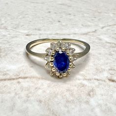 Vintage 10 Karat Yellow Gold Synthetic Blue Stone & Diamond Halo Ring - WeilJewelry Oval Sapphire Ring With Halo Setting In 14k Gold, Blue Oval Birthstone Ring With Diamond Accents, Oval Sapphire Ring With Halo Design In 14k Gold, Oval Sapphire Ring With Halo In 14k Gold, Oval Sapphire Cluster Ring With Center Stone, Gold Oval Sapphire Cluster Ring, Gold Sapphire Oval Cluster Ring, Blue Oval Cluster Ring With Halo Setting, Oval Sapphire Cluster Ring In Gold