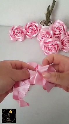 two hands are holding pink roses on a white surface and one hand is tying the ribbon