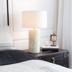 a white lamp sitting on top of a bed next to a night stand with a pillow