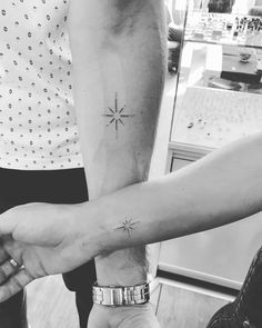 two people are holding hands with tattoos on their arms and one has a small star