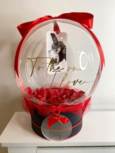 a glass bowl filled with red roses on top of a white table next to a card that says to the one i love