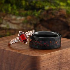 two rings with red stones on them sitting on top of a wooden table next to some rocks