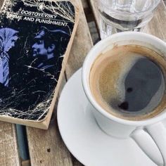 a cup of coffee sitting on top of a wooden table next to an open book