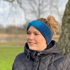 a woman wearing a blue headband standing next to a tree in a grassy field