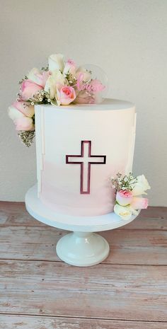 a white cake with flowers and a cross on top is sitting on a wooden table