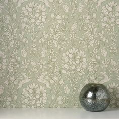 a silver vase sitting on top of a white table next to a green wallpaper