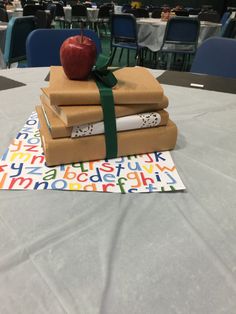 stack of books and an apple on top of each other at a table with tables in the background