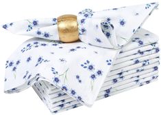 a stack of white napkins with blue flowers and gold ring on each folded napkin