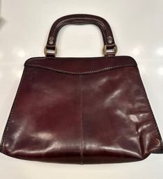 This vintage handbag from the 1970s features two handles and several interior zipper pockets. The tag says it was handmade in Italy with genuine leather. The exterior of the purse is a smooth, shiny patent leather. Measurements: 12 x 10 inches, opening is 10 x 6 inches and is 8 inches deep Condition: Good Formal Handheld Burgundy Satchel, Formal Burgundy Satchel With Handle Drop, Vintage Bags With Leather Lining And Double Handle, Vintage Bags With Double Handle And Leather Lining, Vintage Top Handle Briefcase For Formal Use, Vintage Burgundy Rectangular Satchel, Retro Tote Satchel For Office, Retro Office Satchel Tote, Retro Top Handle Business Satchel