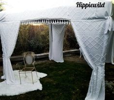 a white tent with curtains and chairs in the grass