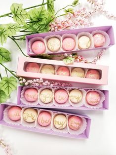 three boxes filled with pink and white macaroons on top of a table next to flowers